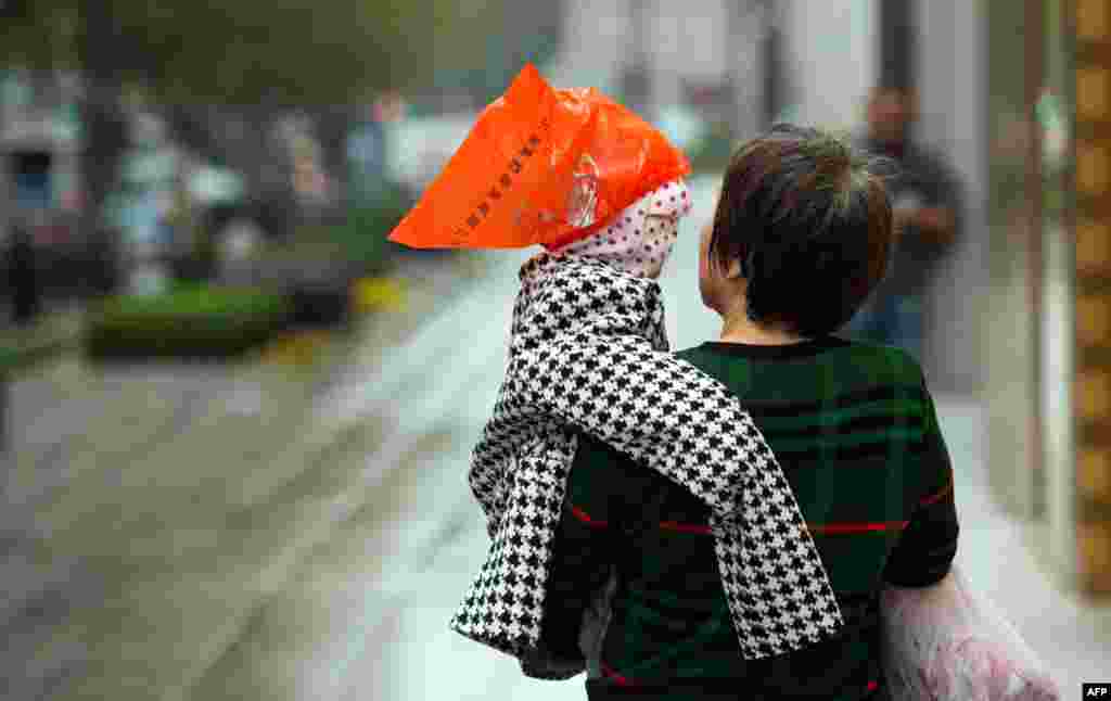 A woman carries a boy covered with a mask and a plastic bag to protect against the rain in Shanghai, China.