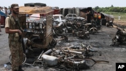 Un soldado pakistaní hace guardia mientras rescatistas examinan el sitio de la explosión de un camión cisterna en una carretera cerca de Bahawalpur, Pakistán, el domingo, 25 de junio de 2017.