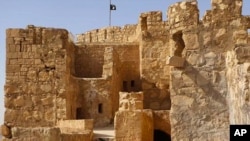 FILE - Photo released by website of Islamic State militants shows the Islamic State group's flag, top center, raised on the top of Palmyra castle, Syria, May 22, 2015.