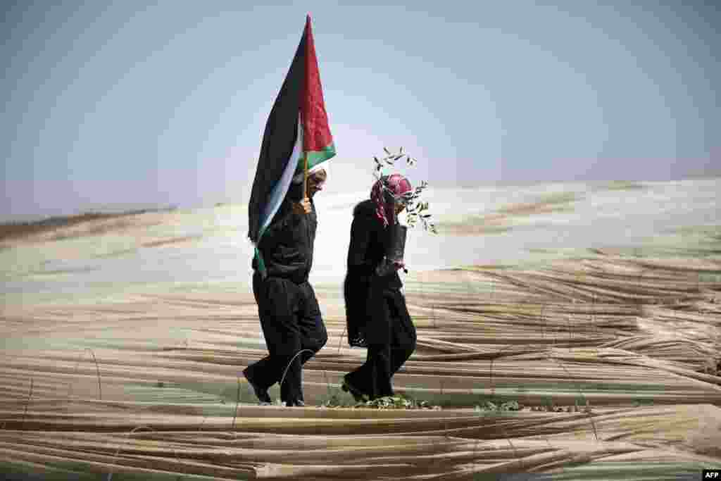 Palestinians, a man holding a Palestinian flag and a woman carrying an olive tree, walk through rows of greenhouses on &quot;Land Day&quot; during which people notably plant olive trees near the Israeli border in Jabalia, in the northern Gaza Strip.