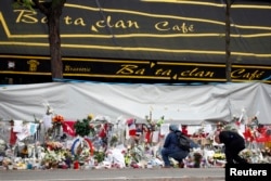 FILE - People mourn in front of the screened-off facade of the Bataclan Cafe adjoining the concert hall, one of the sites of the deadly attacks in Paris, France, a day before a ceremony to pay tribute to the 130 victims, Nov. 26, 2015.