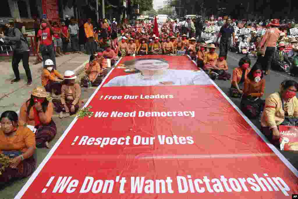 Myanma - Mandalay şəhərində nümayişçilər üzərində həbsdə olan lider Aung San Suu Çinin şəkli olan nəhəng plakatın qarşısında oturaraq çevriliş əleyhinə etiraz aksiyası keçirir.