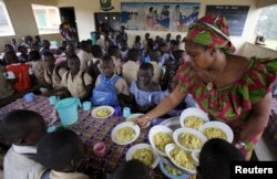 FILE - Students wait to eat at a school canteen, near a sign on the wall that reads "Eating well to learn better," in N'zikro, Aboisso, Ivory Coast, Oct. 27, 2015.