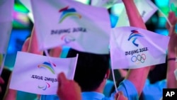 FILE - Participants wave flags with the logos of 2022 Beijing Winter Olympics and Paralympics before a launch ceremony to reveal the motto for the Winter Olympics and Paralympics in Beijing, Sept. 17, 2021. 
