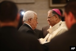 Palestinian President Mahmoud Abbas, left, greets the Latin Patriarch of Jerusalem Fouad Twal during a Christmas Midnight Mass at the Church of the Nativity in the West Bank town of Bethlehem, Dec. 25, 2015.