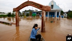 A Cambodian woman pushes a church gate with an oar to steer her wooden boat in a flooded area along the Mekong river in Koh Phos village, Kandal province near Phnom Penh, Cambodia, Sunday, Sept. 29, 2013.