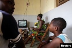 Jean-Noel Kouame joins his family as they watch television inside their house in Abidjan, Ivory Coast, Dec. 18, 2017.