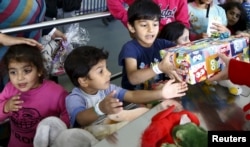 FILE - Migrant children reach out for gifts donated by the local community for the Bayram festivities at an improvised temporary shelter in a sports hall in Hanau, Germany, Sept. 24, 2015.