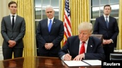 U.S. President Donald Trump, flanked by Senior Advisor Jared Kushner (standing, L-R), Vice President Mike Pence and Staff Secretary Rob Porter signs his first executive orders in the Oval Office Jan. 20, 2017. (REUTERS/Jonathan Ernst )