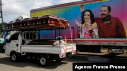 A truck carrying coffins drives past a banner of Nicaragua's President -- and presidential candidate -- Daniel Ortega and his wife and running mate, Rosario Murillo, on a mobile clinic, in Masaya, Nov. 2, 2021.
