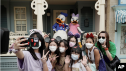 在香港迪士尼樂園，戴著口罩的遊客與標誌性卡通人物唐老鴨和黛絲鴨自拍。 （2020年9月25日）