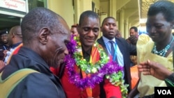 David Emong's parents wrap garlands around his neck at Entebbe International Airport, welcoming him back to Uganda after his Paralympics win. (L. Paulat/VOA)
