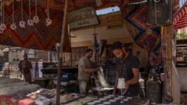 In this May 9, 2020 photo, 28-year-old football defender Mahrous Mahmoud, right, makes Ramadan sweets at a souq, in Manfalut, a town 350 kilometers (230 miles) south of Cairo in the province of Assiut, Egypt. Mahmoud should be on the field at this time of year playing as a defender for Beni Suef, a club in Egypt's second division. But like millions in the Arab world's most populous country, he has been hit hard by the coronavirus pandemic. (AP Photo/Nariman El-Mofty)