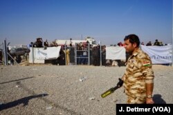 A Kurdish policeman patrols the entrance to the Khasir camp and displaced civilians sure waiting to enter the camp at Khasir.