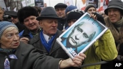 An elderly demonstrator holds a poster showing an edited photo of an aging Prime Minister Vladimir Putin and signed '2050. No'.