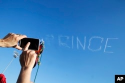 A festival attendee takes a photo as a skywriter spells "Prince," in honor of pop music icon Prince, at the New Orleans Jazz and Heritage Festival in New Orleans, April 23, 2016.