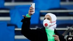 Una aficionada con cubrebocas toma una fotografía con su teléfono celular antes del duelo de los octavos de final de la Liga de Campeones entre el Real Madrid y el Manchester City en el Estadio Santiago Bernabéu de Madrid, el miércoles 26 de febrero de 2020.