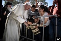 FILE - A child kisses the hand of Pope Francis during a visit at the Moria refugee camp on the island of Lesbos, Greece, April 16, 2016.