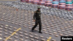 A Colombian police officer walks near packs of confiscated marijuana and cocaine. 