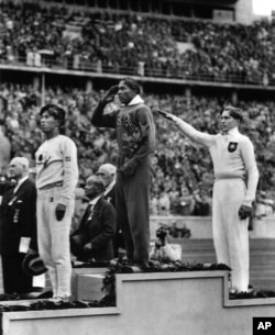 FILE - Jesse Owens, center, salutes during the presentation of his gold medal for the long jump, after defeating Nazi Germany's Lutz Long, right, during the 1936 Summer Olympics in Berlin.