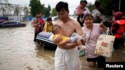 河南省郑州市一名男子怀抱婴儿涉水而行。（2021年7月22日）