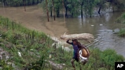 An Indian woman carries her belongings to higher ground after floodwaters swept her temporary tent in Srinagar, India, Sept. 5, 2014.