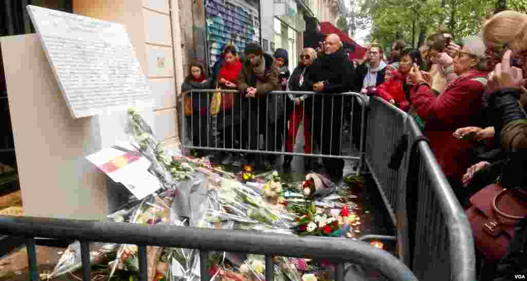 Warga berkumpul di depan plakat yang baru diresmikan di depan gedung konser Bataclan, Paris, tempat serangan maut yang menewaskan 90 orang tahun lalu (13/11). (VOA/L. Bryant)