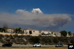 A plume of smoke from a wildfire burning near the Holy Jim area looms, Aug. 6, 2018, in Lake Forest, Calif. Authorities have evacuated cabins in two communities in the Santa Ana Mountains in Orange County because of a fast-moving wildfire.
