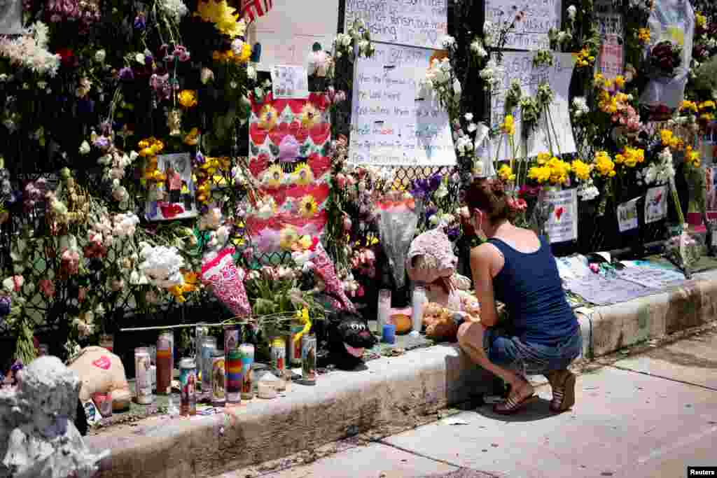 A woman kneels at a memorial site in front of a partially collapsed residential building as the emergency crews continue the search and rescue operations for survivors, in Surfside, Florida, July 3, 2021.