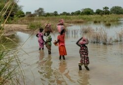 FILE - Children carry bags on their head as they walk through the flooded fields near Malualkon in Northern Bahr el Ghazal State, South Sudan, Oct. 20, 2021.
