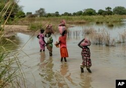 FILE - Children carry bags on their head as they walk through the flooded fields near Malualkon in Northern Bahr el Ghazal State, South Sudan, Oct. 20, 2021.