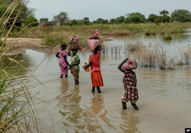 FILE - Children carry bags on their head as they walk through the flooded fields near Malualkon in Northern Bahr el Ghazal State, South Sudan, Oct. 20, 2021.