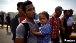 Un migrante salvadoreño que viaja a los Estados Unidos lleva a su hijo en la frontera entre Guatemala y México, en Tecun Uman, Guatemala, el 18 de enero de 2020.