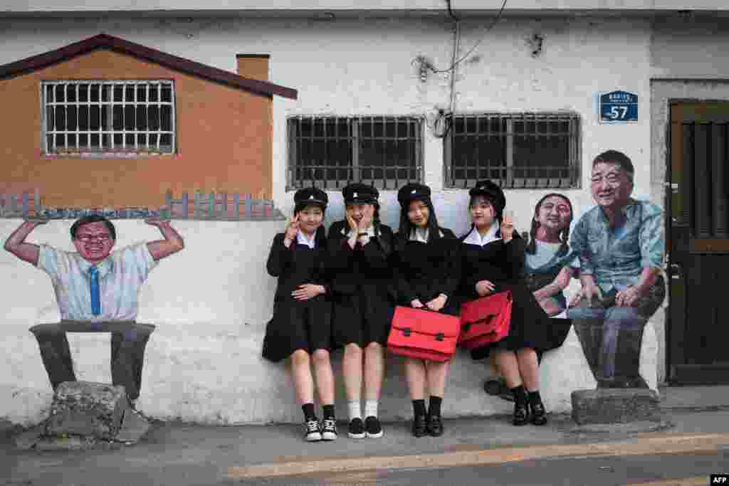 A group of students pose for a photo wearing 1970's style school uniforms as part of an educational initiative available to visitors to the Naksan 'art village' in Seoul.