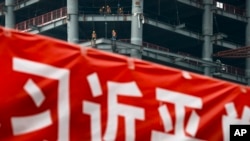 In this April 16, 2017 photo, workers prepare to load cables at a building construction site as a propaganda banner reads "The Party Secretary General Xi Jinping" on display at the Central Business District in Beijing.