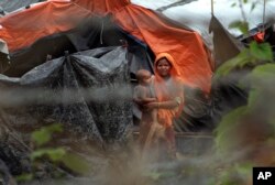 In this June 29, 2018, photo, Rohingya refugees look out from their camp near a fence during a government organized media tour to a no-man's land between Myanmar and Bangladesh