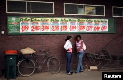 Women chat near posters advertising food prices outside a shop in Harare, Zimbabwe, Nov. 25, 2017.