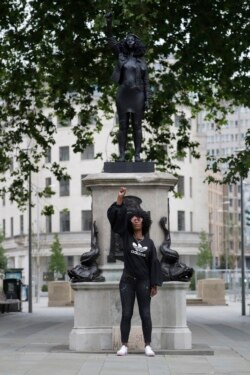Jen Reid berpose di depan resin hitam dan patung baja baru yang menggambarkan dirinya, yang diberi judul "A Surge of Power (Jen Reid) 2020" karya seniman Marc Quinn, di Bristol, Inggris, 15 Juli 2020.