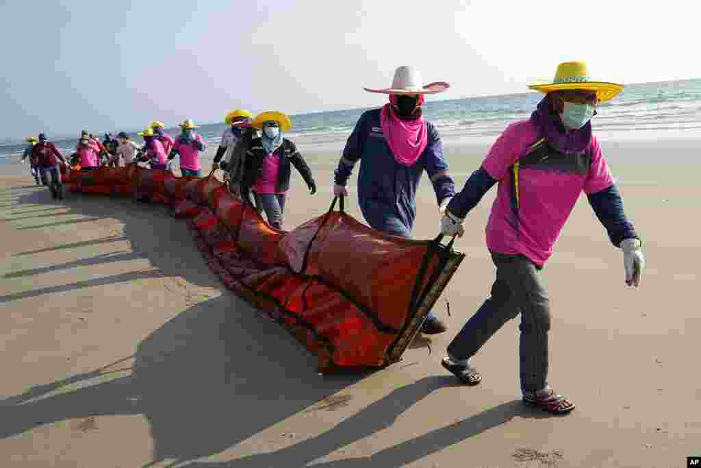 Workers drag an oil spill boom out onto Mae Ram Phueng Beach in hopes of containing any oil washing up from a recent spill off the coast of Rayong, eastern Thailand.