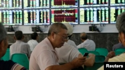 An investor uses his mobile phone in front of electronic screens showing stock information at a brokerage house in Wuhan, Hubei province, August 16, 2013. 