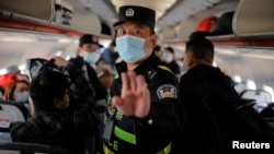 FILE - A police officer orders Reuters journalists off the plane before all other passengers without explanation while the plane is parked on the tarmac at Urumqi airport, Xinjiang Uyghur Autonomous Region, China, May 5, 2021. 