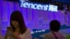 FILE - A woman uses her smartphone near a booth for the Chinese Internet company Tencent at the Global Mobile Internet Conference in Beijing, China, April 29, 2015.