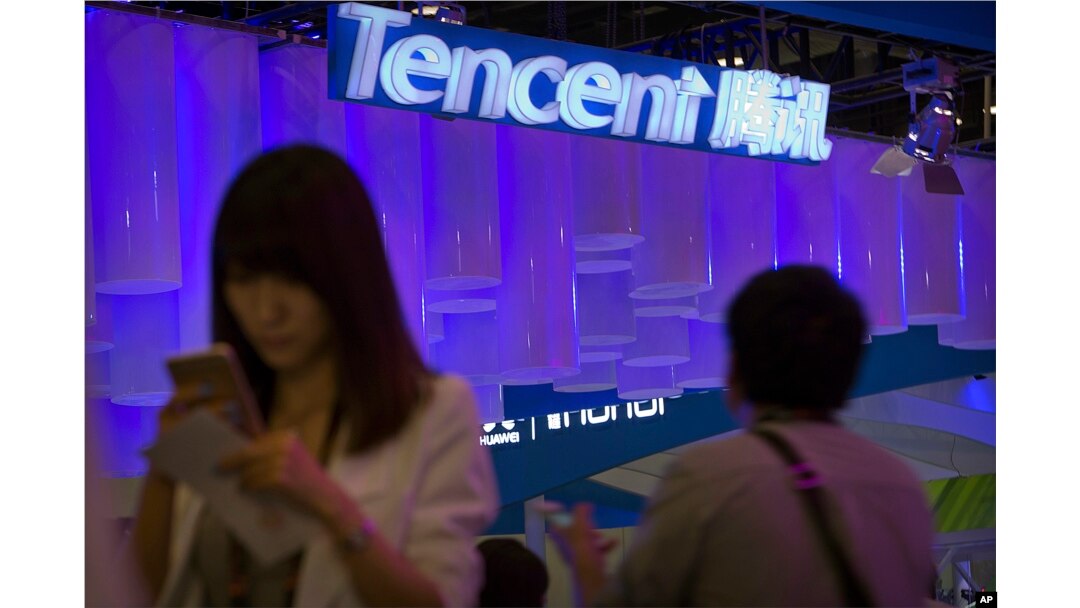 FILE - A woman uses her smartphone near a booth for the Chinese Internet company Tencent at the Global Mobile Internet Conference in Beijing, China, April 29, 2015.
