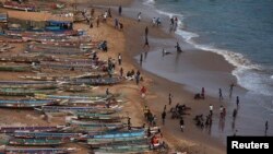 Photo d’archives : des gens sont photographiés sur une plage à côté de pirogues de pêche à Dakar, au Sénégal, le 21 juin 2013.