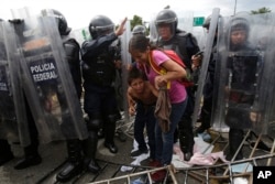A Honduran migrant mother and child coweras they are surrounded by Mexican Federal Police in riot gear, at the border crossing in Ciudad Hidalgo, Mexico, Oct. 19, 2018.