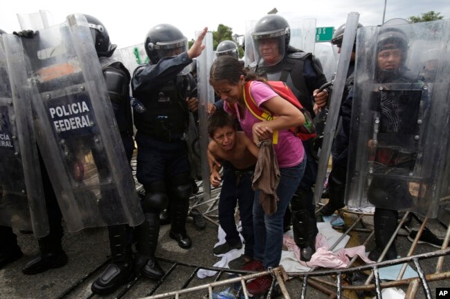 A Honduran migrant mother and child cower as they are surrounded by Mexican Federal Police in riot gear, at the border crossing in Ciudad Hidalgo, Mexico, Oct. 19, 2018.