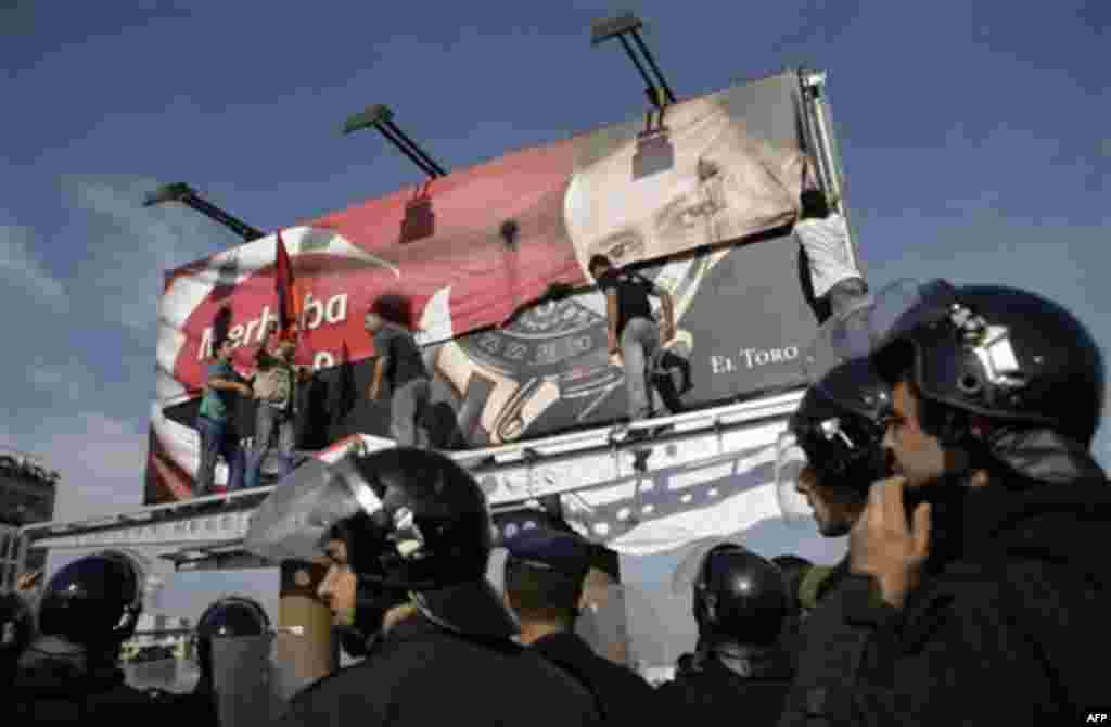 Lebanese men of Armenian descent, tear up a poster showing Turkish Prime Minister Recep Tayyip Erdogan as they protest against his visit, as riot police watch, in Beirut's Martyrs' Square, Lebanon, Thursday, Nov. 25, 2010. (AP Photo/Grace Kassab)