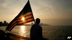 Un estudiante mexico-estadounidense que estudia en Cuba observa el atardecer en el Malecón de La Habana, ondeando una bandera de Estados Unidos.