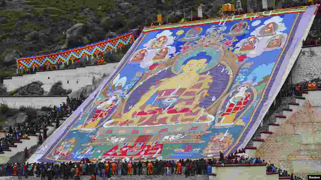 Pemeluk agama Budha dan para turis menyaksikan Thangka berukuran besar yang menampilkan potret Budha pada Festival Shoton di biara Drepung di Lhasa, Wilayah Otonom Tibet di China. Thangka adalah ulaman sutra yang memiliki nilai religius bagi pemeluk Budha di Tibet.