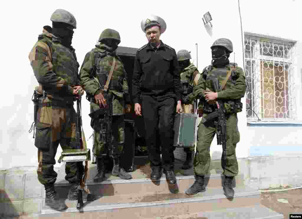 Seorang tentara angkatan laut Ukraina melewati pria-pria bersenjata yang diduga kuat tentara Rusia, saat meninggalkan markas besar Angkatan Laut di Sevastopol, 19 Maret 2014.